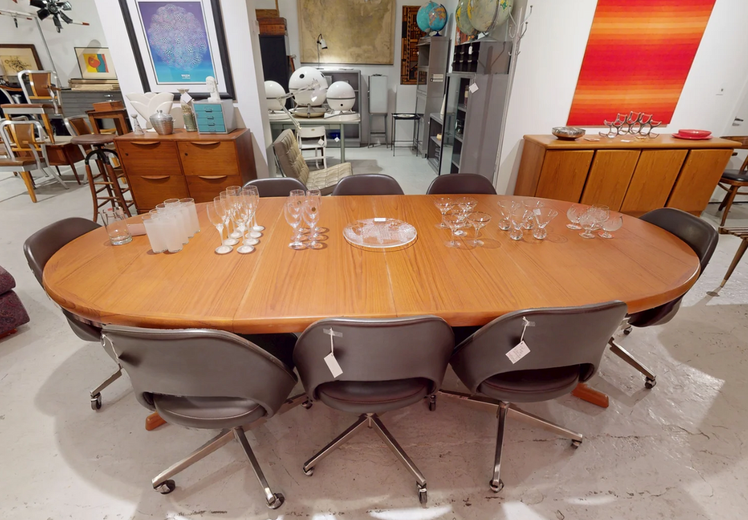 Oval teak dining table with two extension leaves surrounded by chairs